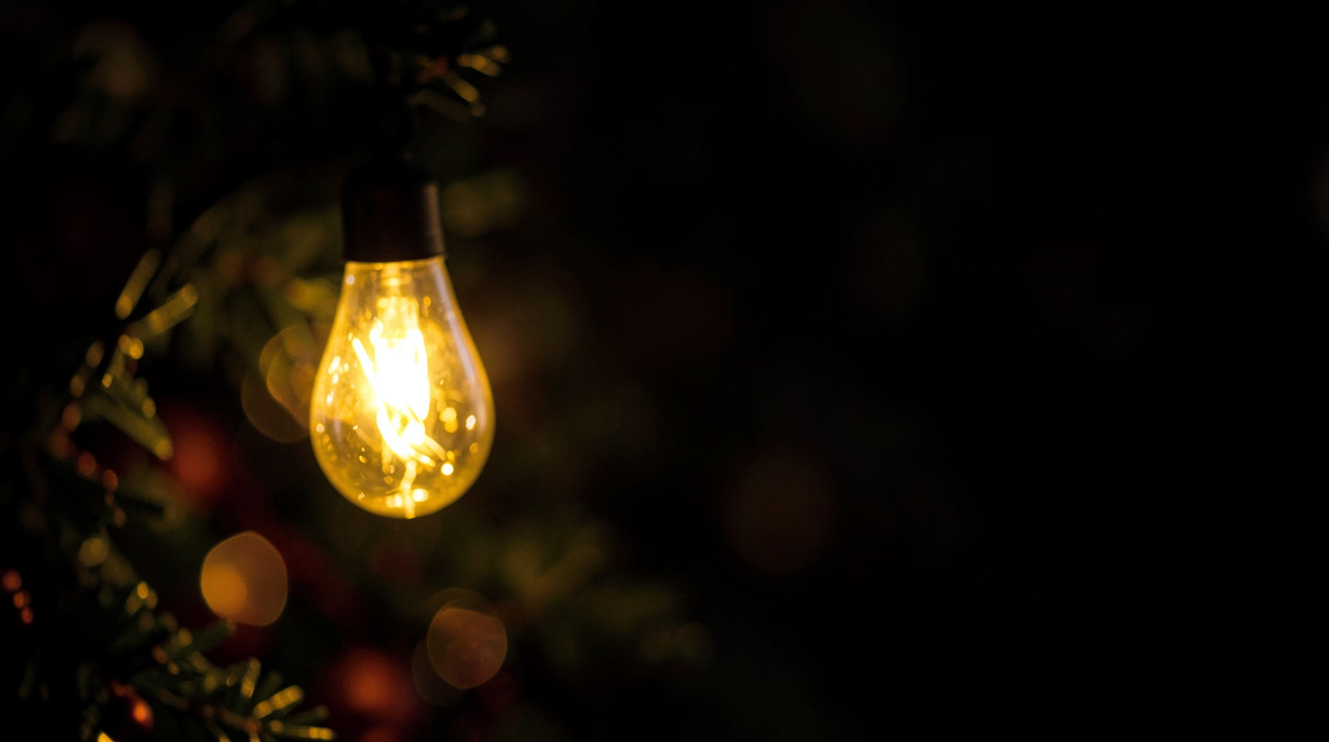 Close-up of a single golden Christmas light with a bokeh effect, set against a dark background and warm lighting.