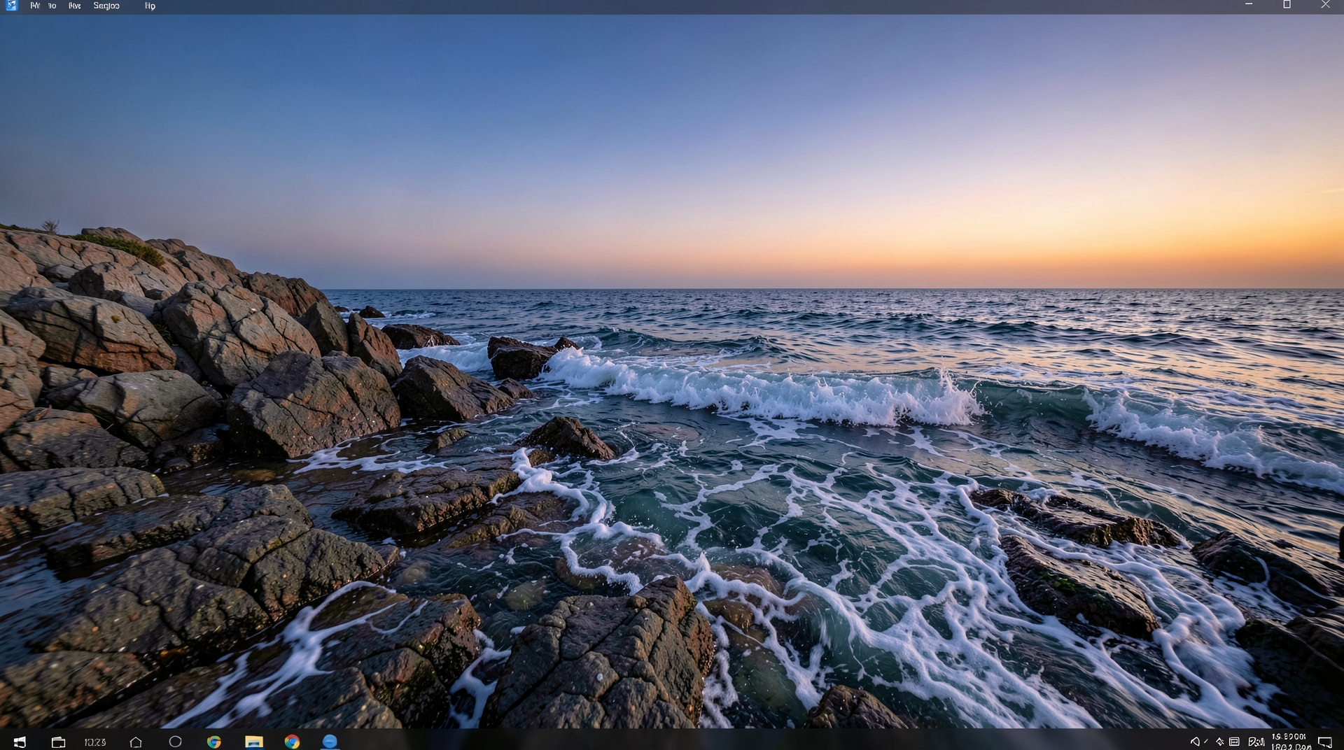 A rocky coastline at dusk with gentle waves crashing against the shore.